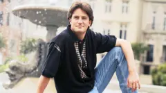 Matthew Perry poses for a portrait on a fountain, wearing blue jeans and a polo shirt
