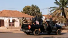 Armed men wearing camouflage fatigues drive a truck through the streets
