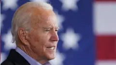 Joe Biden com bandeira americana ao fundo