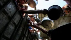 Palestinci drže posude u koje im se sipa humanitarna pomoć