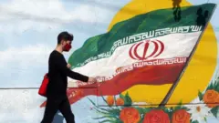 An Iranian boy walks past a mural with Iran's national flag