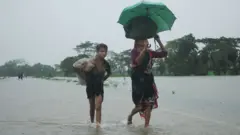 প্রবল বৃষ্টির মধ্যে নিরাপদ আশ্রয়ের সন্ধানে ছুটছে সিলেটের বন্যা আক্রান্ত মানুষ