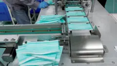 Esteira de fabricação com máscaras e mãos com luvas ao fundo