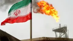 A gas flare on an oil production platform in the Soroush oil fields is seen alongside an Iranian flag in the Persian Gulf, Iran, in July 2005
