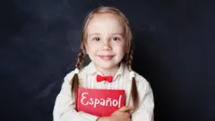 Niña sostiene un libro con la palabra español.