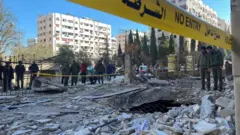 Police officers stand on the rubble of a damaged building at the site of a rocket attack, in central Damascus' Kafr Sousa neighborhood, Syria, February 19, 2023