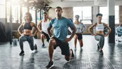 A group of people perform lunges in a gym class