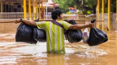 थाईल्यान्डमा भारी बोकेर जलमग्न सडक पार गर्दै एक मानिस