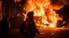Un manifestante delante de un contenedor de basura en llamas.