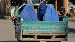Burqa-clad women travel in a vehicle along a street in Kandahar on 18 December