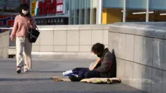 A woman wears a face mask as she walks past a homeless man in Osaka, Japan
