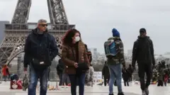 Pessoas de máscara diante da Torre Eiffel