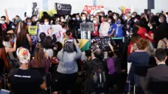 Dezenas de pessoas reunidas em volta de palanque, segurando bandeiras diversas de movimentos sociais, entre outros