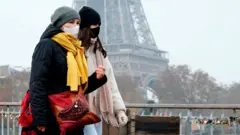 Abagore babiri batambuka n'amaguru iruhande y'umunara wa Tour Eiffel mu Bufaransa