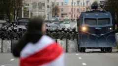 A protester with a flag stands in front of Belarusian policemen and a water cannon that block a road during a rally against government and President Lukashenko in Minsk, Belarus, 25 October 2020