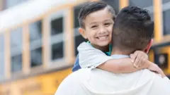 Niño sonríe mientras se abraza al cuello de un hombre