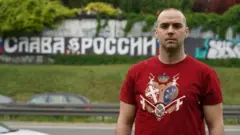 Damjan Knezevic stands in front of a Belgrade street graffiti that reads 'Glory to Russia' in Russian
