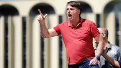 Bolsonaro faz gesto com a mão falando a manifestantes em área externa em Brasília