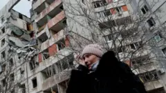 Una mujer frente a un edificio dañado en Mariúpol