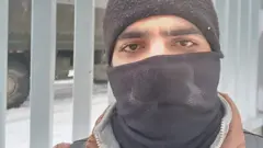 Abdulrahman Kiwan wearing grey balaclava standing in front of a fence