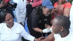 Minisitiri w'ubuzima Dr Diane Gashumba (wambaye ingofero) akingira umwe mu baturage kuri iki cyumweru