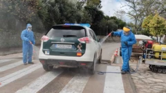 Pessoas com roupas de proteção e máscaras limpando um carro