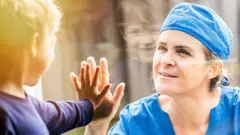 A health worker and her son are separated by a window - they both put up their hands to touch through the glass