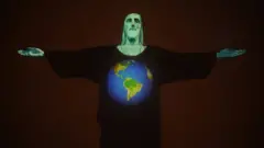 Estátua do Cristo Redentor à noite, iluminada por projeção mostrando um desenho do planeta em homenagem a vítimas da covid-19