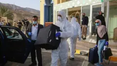A worker helps a mask-clad woman with her baggage