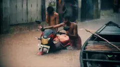 Dois homens arrastam moto em enchente