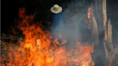 Un hombre detrás de las llamas en la selva amazónica.