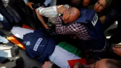 Journalists react next to di body of Al Jazeera correspondent Shireen Abu Aqleh, wey dem shoot dead during one Israeli raid for di occupied West Bank city of Jenin (11 May 2022)