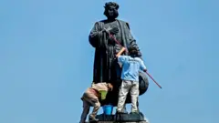 Municipal workers clean a statue of Christopher Columbus, which was protected by a metal fence after activists called to tear it down on social networks, in Mexico City, on October 12, 2020.
