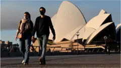 People wearing masks walk past the Sydney Opera House during a state-wide lockdown in August 2021