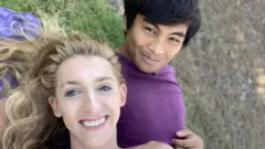 Daniella e Josh deitados na grama e sorrindo para foto