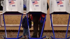 Un enfant regarde la caméra pendant qu'un parent vote lors des élections de mi-mandat américaines de 2018.
