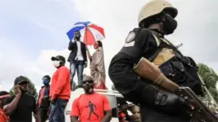 Ku wa mbere, Bobi Wine, umunyamuziki akaba n'umunyapolitike urimo kwiyamamariza kuba Perezida wa Uganda, ahagaze hejuru y'imodoka ageza ijambo ku bitabiriye mitingi ye mu mujyi wa Fort Portal.