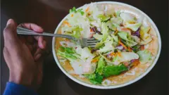 Une main qui tient une fourchette dans un plat de salade