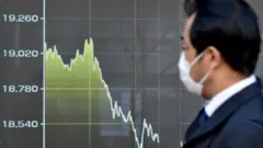 Tokyo'da Nikkei endeksindeki düşüşü gözlemleyen bir Japon