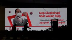 Dua warga melintasi papan informasi terkait vaksinasi COVID-19 di Jakarta, Kamis (31/12/2020).