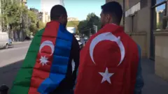 Два парня на дороге. У одного на плечах азербайджанский флаг, у другого - турецкий.