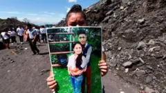 Una mujer sostiene la foto de unos familiares que murieron por la erupción del Volcán de Fuego el 3 de junio de 2018 en el primer aniversario de la tragedia en San Miguel Los Lotes, Guatemala.