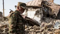 শুষা শহরে বিধ্বস্ত একটি বাড়ির সামনে দাঁড়িয়ে ধ্বসংস্তুপের দিকে তাকিয়ে আছেন স্থানীয় এক ব্যক্তি।