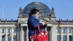 Woman walks past Reichstag wearing a mask