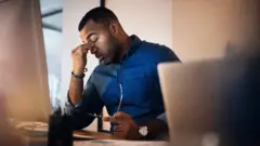 Man holds head in his hands at a desk