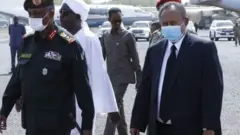 Prime Minister of Sudan, Abdalla Hamdok (C) wears a face mask as a preventive measure against the coronavirus (Covid-19) pandemic as he attends the official funeral ceremony of Sudan's Defense Minister Gamal Omer, 59, died in Juba, the capital of neighboring South Sudan, at Khartoum International Airport on March 25, 2020 in Khartoum