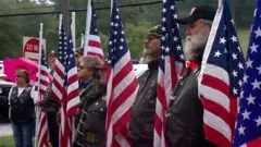 Veteranos enfileirados em cerimônia, ao lado de bandeiras dos EUA