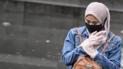 Seorang perempuan berjalan menggunakan masker dan sarung tangan plastik di Jakarta, Senin (06/04).