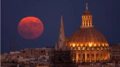 The Sturgeon Supermoon rises behind the steeple of St Paul's Anglican Pro-Cathedral and the dome of the Basilica of Our Lady of Mount Carmel in Valletta, Malta
