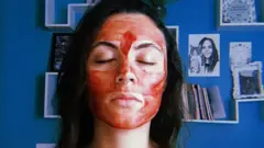 A picture of 27-year old Laura Mocellin Teixeira with her eyes closed, and her face and chest painted with menstrual blood